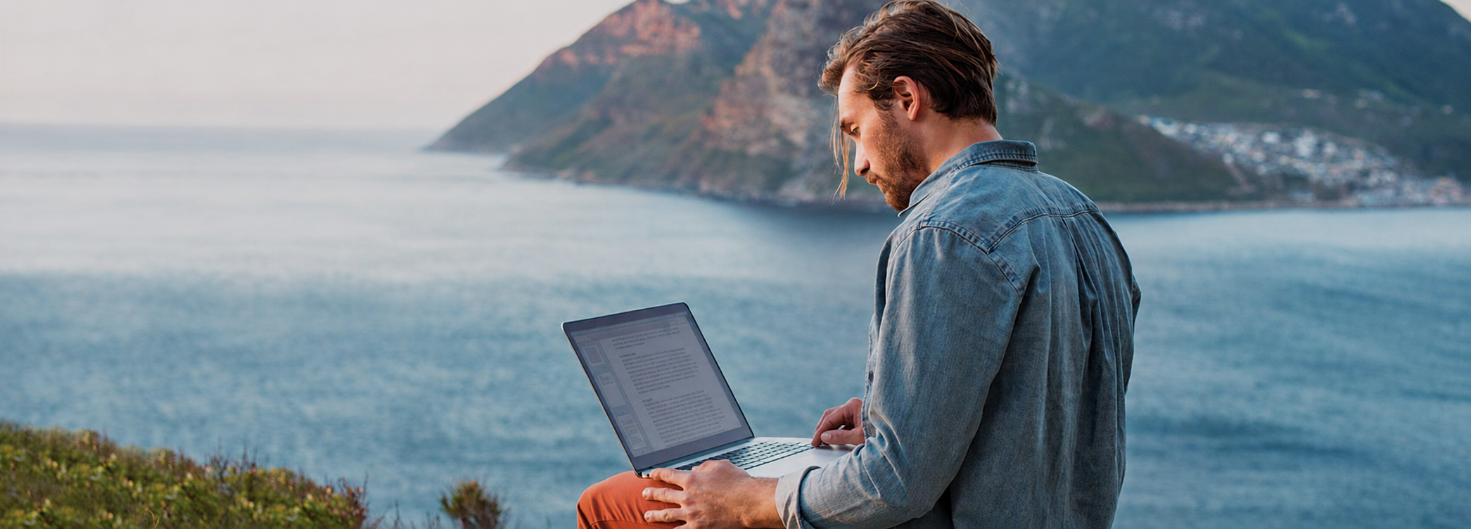 Person working on a laptop with a scenic coastal view — Bitdefender Central setup guide